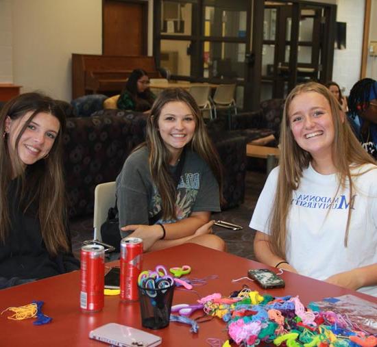 three students smiling for a photo as they are doing crafts 